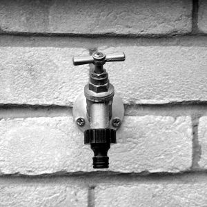 Black and white photo of a metal water faucet on a brick wall, emphasizing texture.