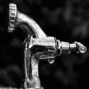A detailed black and white image showcasing a chrome water faucet with water droplets.