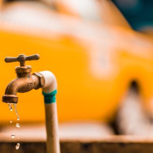 Macro shot of a brass faucet with water droplets against a blurred yellow background.